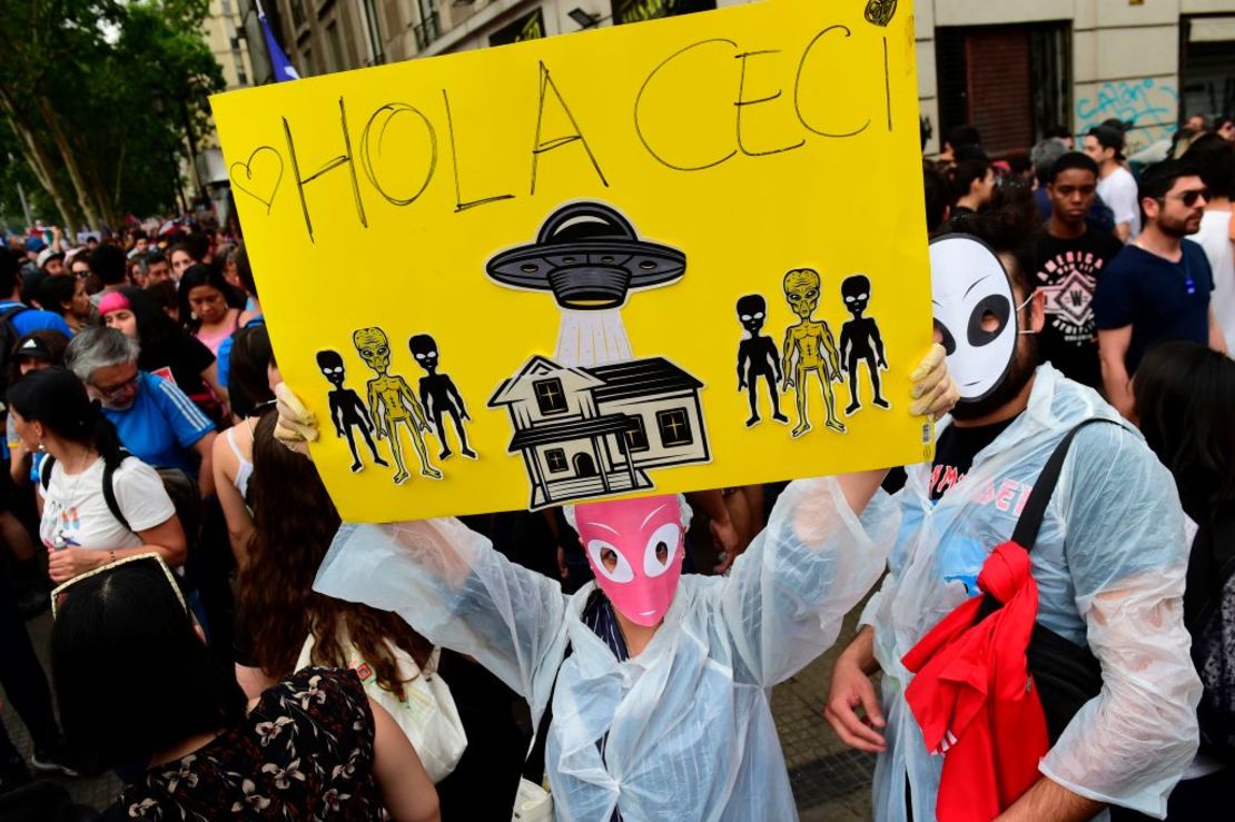 Un manifestante enmascarado sostiene un cartel que representa a extraterrestress y lee "Hola Ceci", refiriéndose a la primera dama chilena, Cecilia Morel, y sus comentarios sobre las protestas.