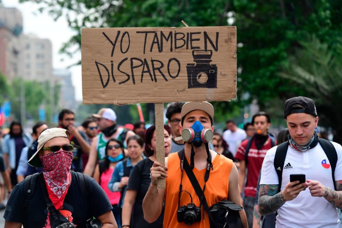 Un hombre sostiene un cartel que dice "Yo también disparo", con el dibujo de una cámara.