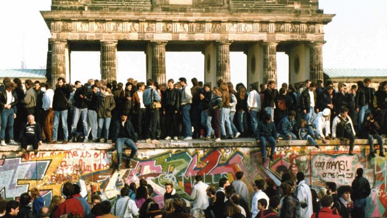 Personas caminan sobre el Muro de Berlín frente a la Puerta de Brandenburgo el 10 de noviembre de 1989. AP