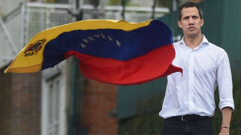 Juan Guaidó, presidente de la Asamblea Nacional de Venezuela y reconocido como presidente interino por más de 50 países, despliega una bandera venezolana frente a la embajada de Bolivia en Caracas.