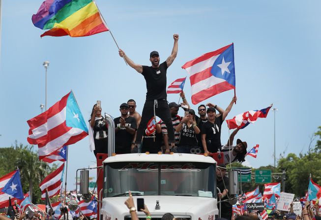 El cantante Ricky Martin, ondeando una bandera del arco iris, se une a las protestas en San Juan, Puerto Rico, el 22 de julio. El gobernador puertorriqueño Ricardo Rosselló renunció después de más de una semana de protestas. Los manifestantes comenzaron a pedir la renuncia de Rosselló después de que el Centro de Periodismo de Investigación de Puerto Rico publicara una serie de mensajes homofóbicos y misóginos entre Rosselló y miembros de su círculo íntimo. Las filtraciones se produjeron la misma semana en que dos exfuncionarios de la administración de Rosselló fueron arrestados como parte de una Investigación de corrupción federal.