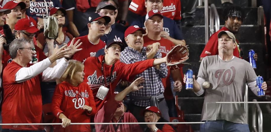 El fanático de los Nationals de Washington, Jeff Adams, con dos cervezas en la mano, deja que una pelota de cuadrangular lo golpee en el pecho durante el Juego 5 de la Serie Mundial el 27 de octubre. El sacrificio de Adams se volvió viral, y Bud Light le dio boletos para el Juego 6 en Houston.