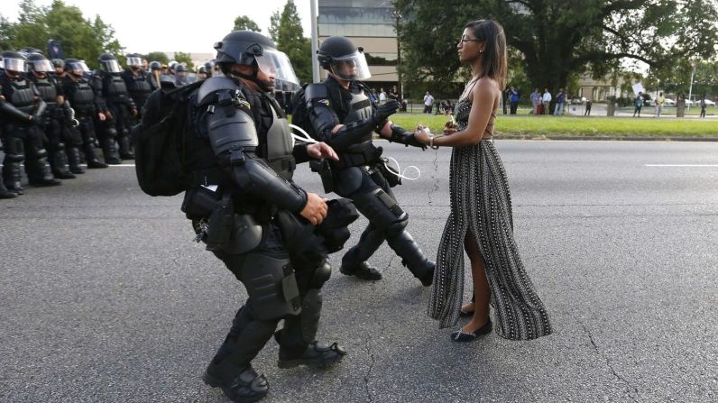 La activista Ieshia Evans se mantiene en la calle en julio de 2016 mientras dos policías se dirigen a arrestarla cerca de la sede del Departamento de Policía de Baton Rouge en Louisiana. Ella fue una de los cientos de manifestantes que bloquearon una carretera de Baton Rouge para denunciar la brutalidad policial. Alton Sterling, un hombre negro de 37 años, fue asesinado a tiros por uno de los dos policías blancos que lo enfrentaron afuera de una tienda de conveniencia de la ciudad. El video del teléfono celular mostró a Sterling sujetado al suelo por los agentes antes de que le dispararan; la policía dijo que Sterling recibió disparos porque estaba tratando de alcanzar una pistola.