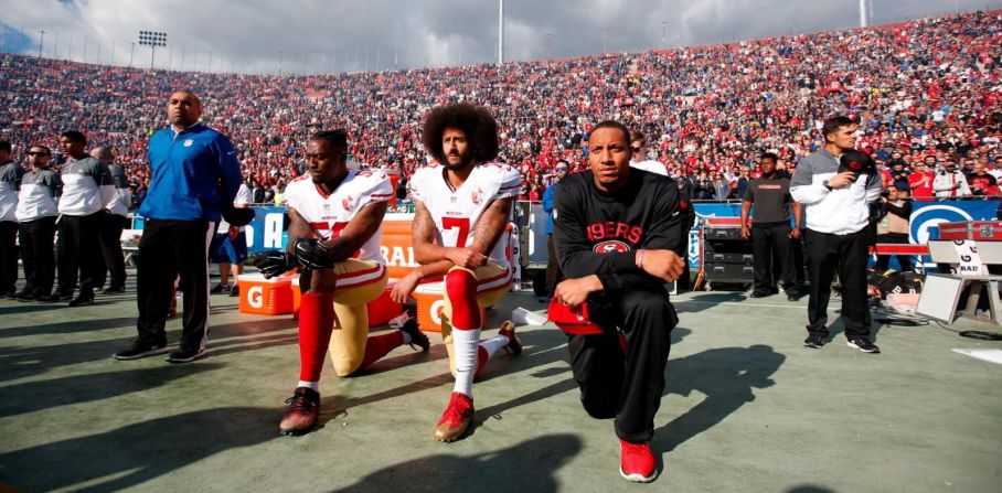 De izquierda a derecha, los jugadores de San Francisco 49ers Eli Harold, Colin Kaepernick y Eric Reid se arrodillan durante el himno nacional en diciembre de 2016. A lo largo de toda la temporada, Kaepernick se negó a estar de pie durante el himno nacional porque no quería “mostrar orgullo por la bandera de un país que oprime a los negros y a las personas de color”. Un creciente número de jugadores de la NFL se le unió y comenzaron a arrodillarse o levantar los puños durante el himno, pero los críticos percibieron las protestas como antipatrióticas e irrespetuosas con la bandera estadounidense y el Ejército del país.