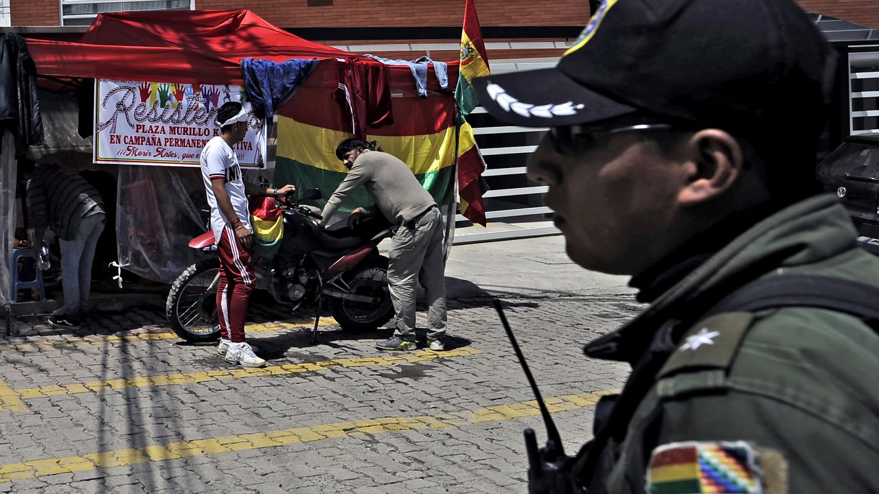 A policeman stands guard as opponents of Bolivian ex-president Evo Morales, exiled in Argentina, camp outside La Rinconada gated community, where the Mexican embassy is located, in La Paz on Dcember 30, 2019. - Bolivia's interim president, Jeanine Anez, announced Monday that the country will expel Mexico's ambassador and two Spanish diplomats, escalating a dispute over an alleged attempt to extract an ex-government aide. (Photo by JORGE BERNAL / AFP)