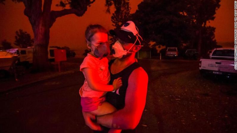 Un padre carga a su hija mientras el cielo se pone rojo durante el día, el 4 de enero en Mallacoota, Australia. Muchos padres con niños pequeños se quedaron atrapados en Mallacoota después de que los vuelos se suspendieran debido al humo y solo a los niños en edad escolar y mayores se les permitió evacuar en barco. Justin McManus / The Age / Fairfax Media a través de Getty Images