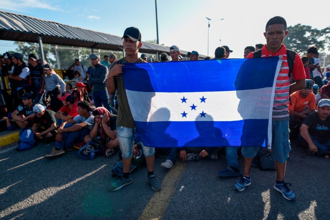 Inmigrantes hondureños que viajan en una caravana hacia Estados Unidos sostienen una bandera de su país mientras esperan el ingreso a México en el Puente Internacional Rodolfo Robles que une Tecum Uman, en Guatemala, con Ciudad Hidalgo, Mexico, el 20 de enero de 2020.