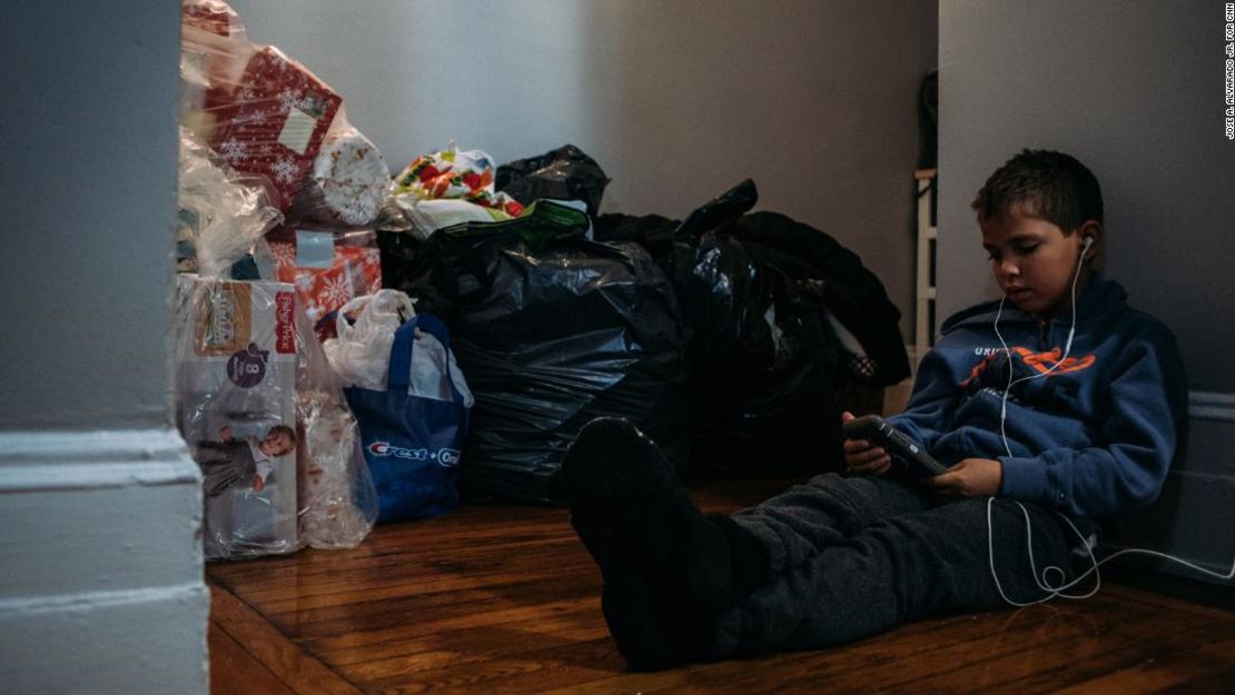 Sebastián Quiñones, de 10 años, mira un video en un teléfono en un pasillo del apartamento de Nueva York de su tía, en medio de un montón de donaciones de ropa para los recién llegados de Puerto Rico. Foto: José A. Alvarado Jr.