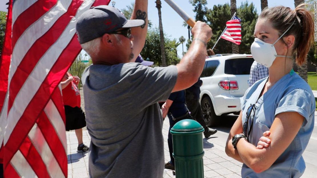 Una trabajadora de la salud permanece de pie en rechazo a la protesta el 20 de abril, mientras personas marchan hacia el Capitolio de Arizona para manifestarse contra la orden de confinamiento del gobernador Doug Ducey por el coronavirus.