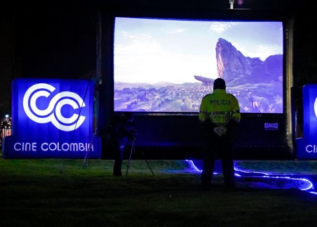 Un policía observa una película proyectada en una pantalla gigante en un parque para que las personas en cuarentena puedan verla desde los balcones. La escena ocurrió en el sector de La Felicidad, en el occidente de Bogotá, Colombia.