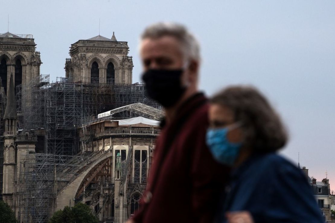 People wearing a face mask walk by Notre Dame cathedral in Paris on April 24, 2020, as the country is under lockdown to stop the spread of the Covid-19 pandemic caused by the novel coronavirus. (Photo by JOEL SAGET / AFP)