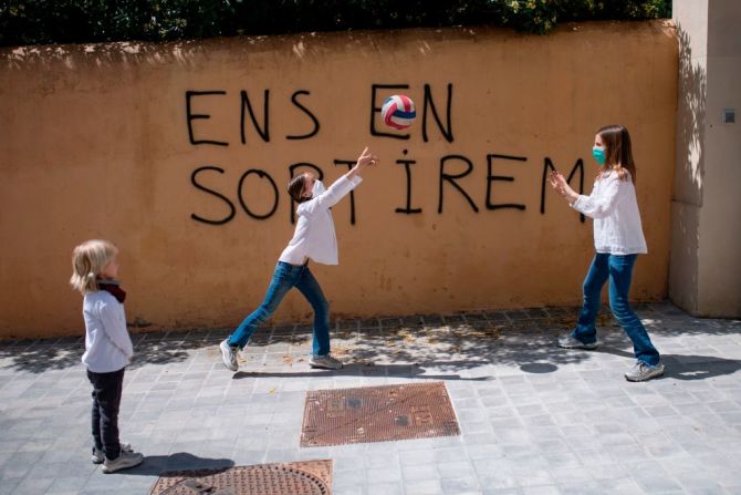 Niñas juegan con tapabocas en Barcelona frente a un graffiti que dice en catalán "Saldremos adelante".