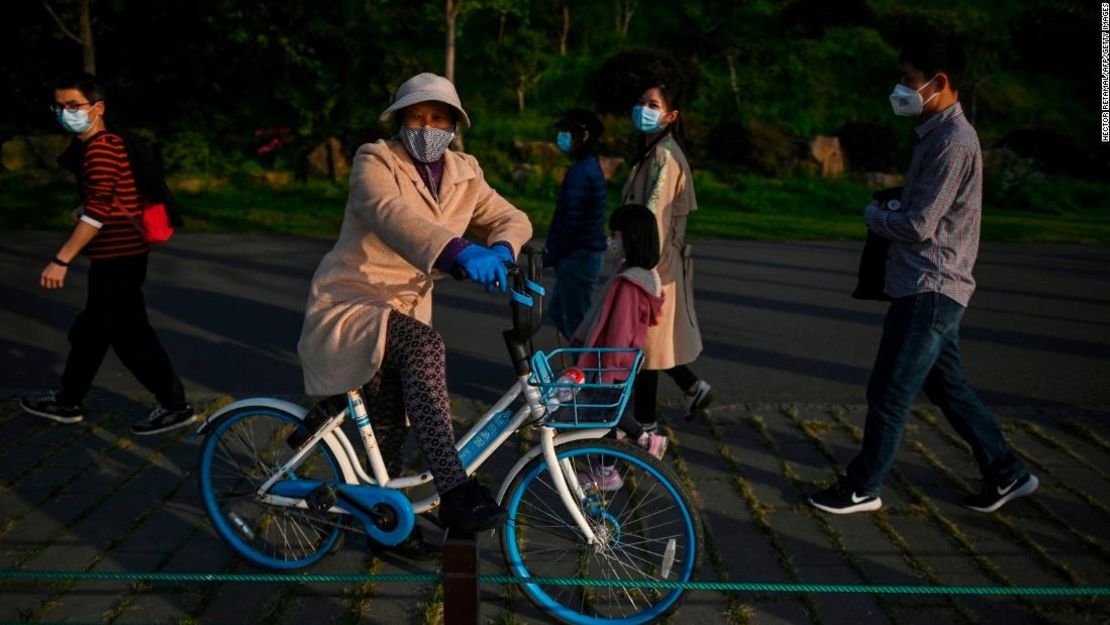 Una mujer con una máscara facial descansa en una bicicleta a lo largo del lago del este en Wuhan después de que se levantó su encierro.