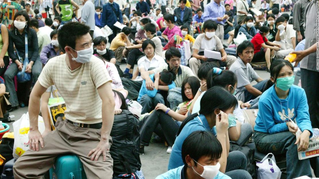 Los trabajadores migrantes con máscaras faciales esperan afuera de la estación de tren en Guangzhou, China, antes de regresar a casa durante el brote de SARS en 2003.