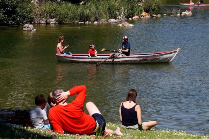 Personas navegan en botes de remos mientras otros se sientan en la hierba en el lago Daumesnil en el bosque de Vincennes en París.