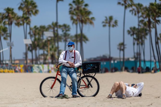 Una mujer toma el sol en la playa en Los Ángeles. Un hombre a su lado usa una máscara.