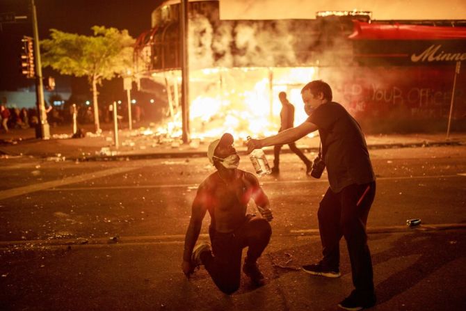 Un manifestante llena de vodka la boca de otro frente a una tienda de licores en llamas en Minneapolis este jueves.