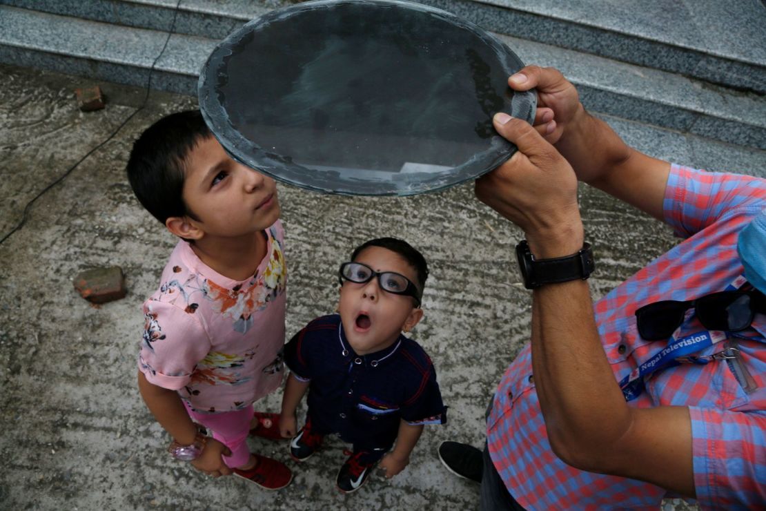 Niños observan el eclipse solar a través de un cristal oscuro en Katmandú, Nepal.