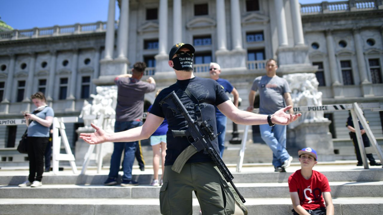 HARRISBURG, PA - MAY 15: A man with an assault rifle reacts while ing demonstrators outside the Pennsylvania Capitol Building to protest the continued closure of businesses due to the coronavirus pandemic on May 15, 2020 in Harrisburg, Pennsylvania. Pennsylvania Governor Tom Wolf has introduced a color tiered strategy to reopen the state with most areas not easing restrictions until June 4.