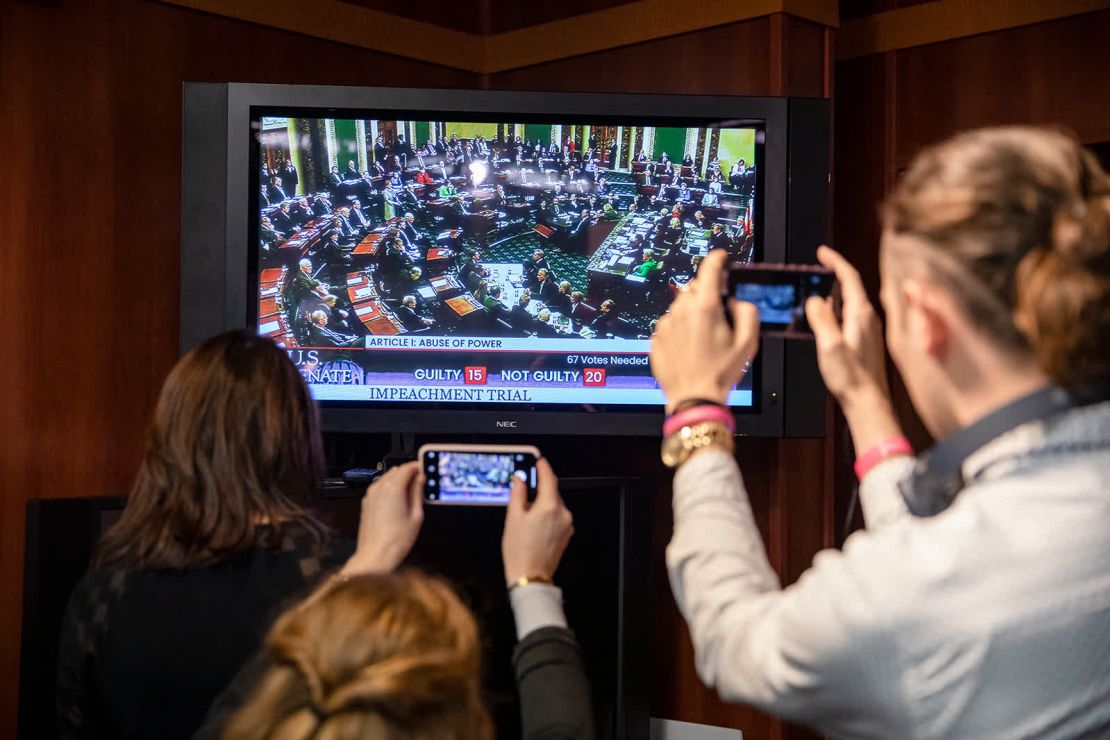 Periodistas en la ciudad de Washington toman fotos a un televisor mientras se transmite la votación del Senado para absolver a Trump.