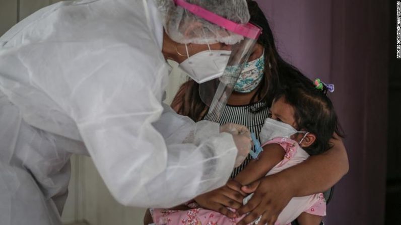Brasil: una madre sostiene a su hija mientras una enfermera con una máscara protectora y una careta le pone a la niña una vacuna contra la gripe. Andre Coelho / Getty Images