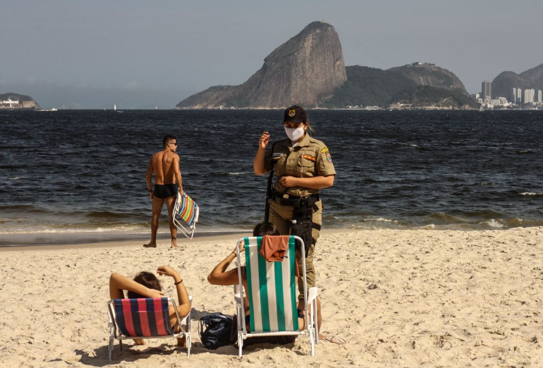 Una policía se acerca a bañistas en la playa Icarai, en Niterói, Brasil, donde está permitido el ejercicio individual pero aún está prohibido usar sillas y carpas.