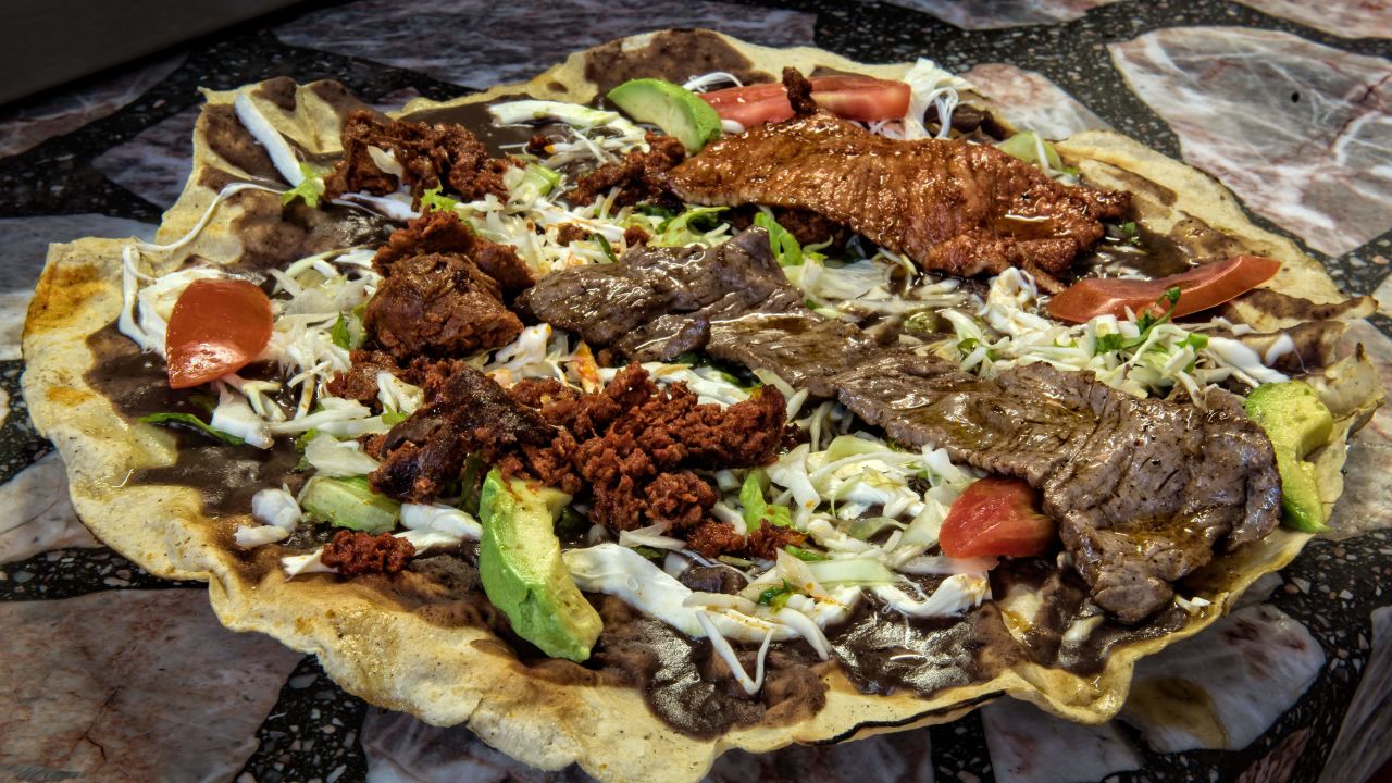 "Tlayuda", platillo típico de Oaxaca preparado con una tortilla grande de maíz, manteca untada, frijoles molidos, queso rallado, jitomate picado, carne seca de res (Tasajo) y chorizo, servido en el restaurante "Chabelita" de Andrea Hernández Cuevas en el mercado "20 de Noviembre", el 23 de febrero de 2017 en Oaxaca, México. Crédito: AFP PHOTO / OMAR TORRES via Getty Images