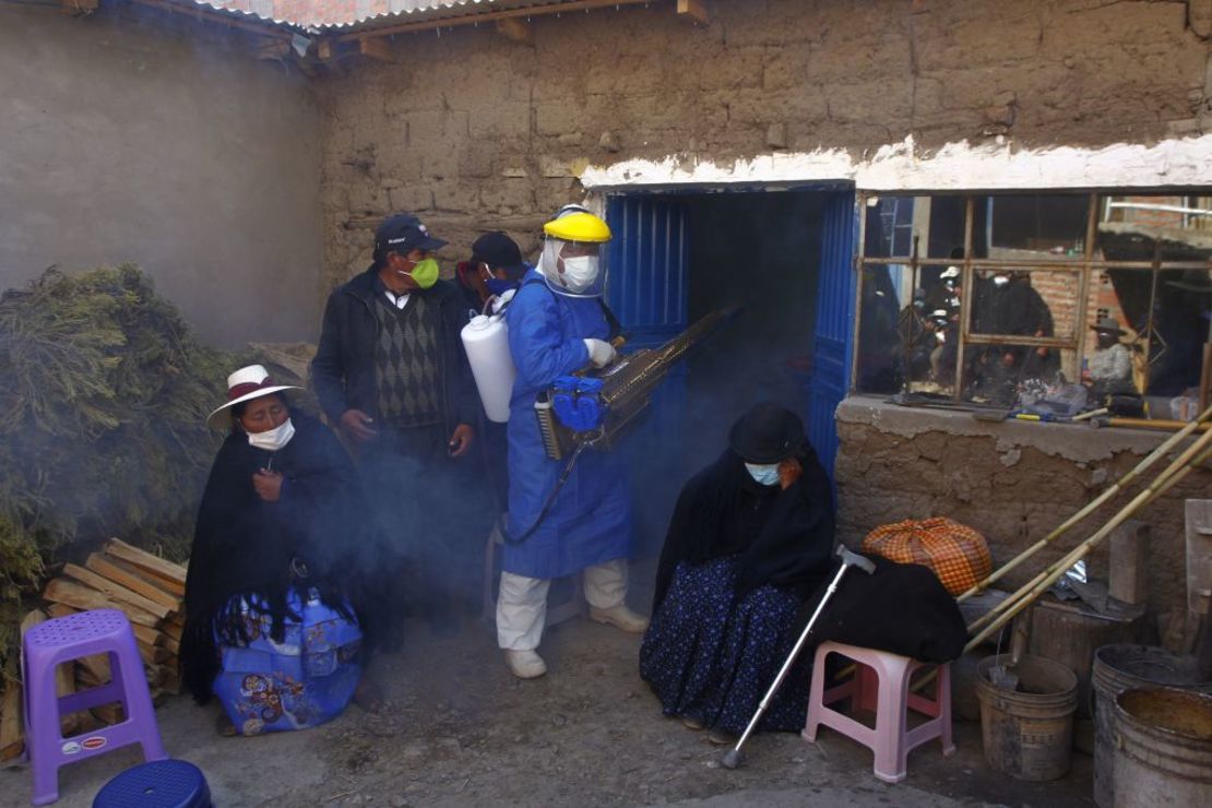 Un empleado funerario con equipo protector desinfecta la casa de una víctima de covid-19 mientras sus familiares siguen en duelo afuera antes de llevar el ataúd al cementerio local en Acora, a una hora de Puno, cerca de la frontera con Bolivia.