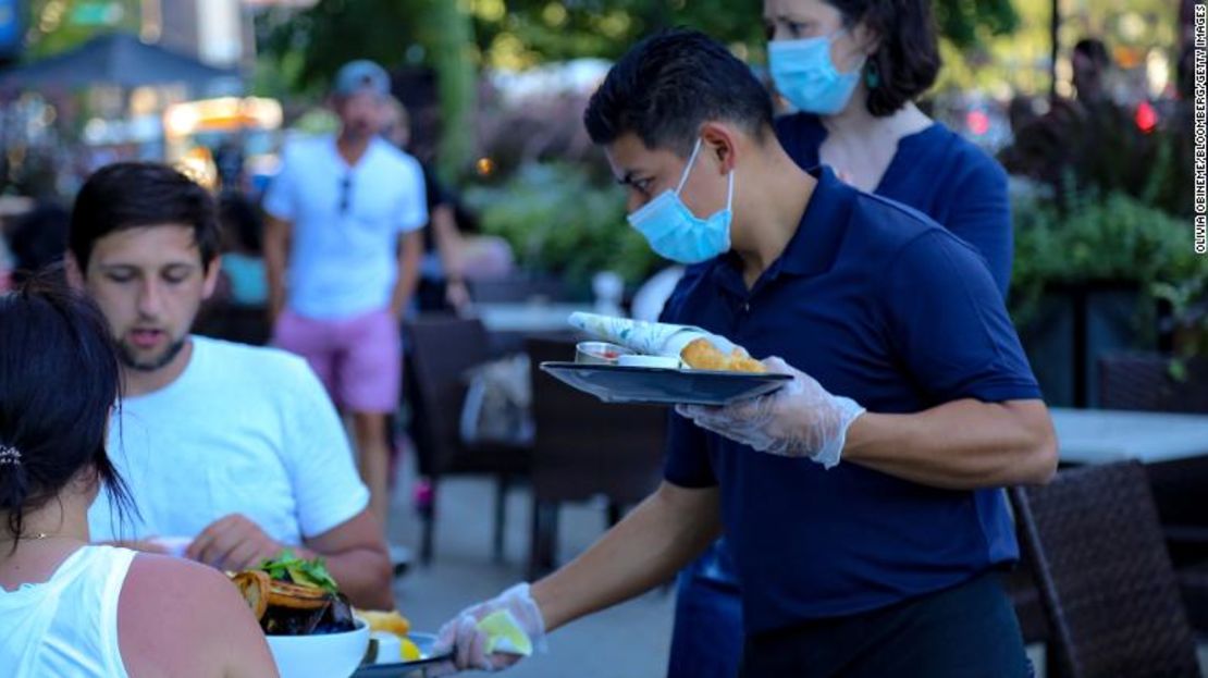 Un mesero con una mascarilla de protección sirve comida a clientes en la zona al aire libre de un restaurante en Chicago en julio pasado.