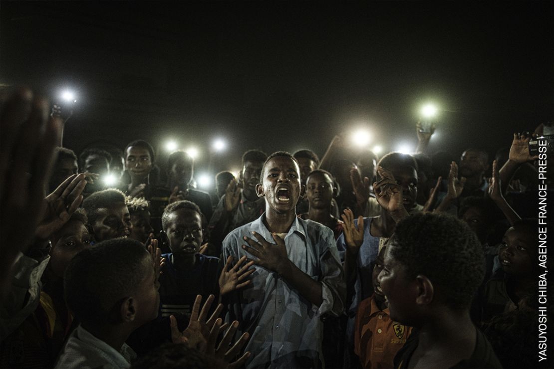 La imagen ganadora presenta a un hombre joven iluminado por teléfonos celulares, recitando poesía de protesta mientras manifestantes entonan consignas a favor de un gobierno civil durante un apagón en Khartoum, Sudán, el 19 de junio de 2019.