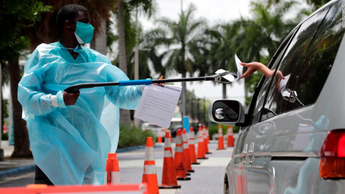 Dante Hills, un trabajador de salud le pasa documentos a una mujer en un vehículo en un sitio de pruebas de covid-19 en Miami.