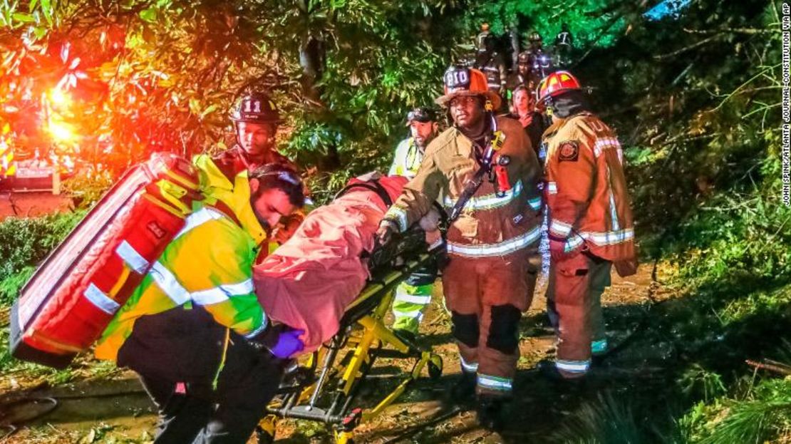 Los bomberos de Atlanta transportan a un hombre que liberaron y que había quedado atrapado en su habitación del tercer piso después de que un árbol cayera en su casa el jueves.