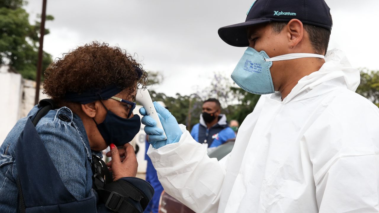 SAO PAULO, BRAZIL - NOVEMBER 02: A cemetery employee using PPE takes the temperature of visitors during the All Souls Day celebrations at the Vila Formosa Cemetery on November 2, 2020 in Sao Paulo, Brazil. The Vila Formosa Cemetery is the largest in Latin America. After months of restricted access due to the coronavirus (COVID-19) pandemic, cemeteries in the city of Sao Paulo are cleared for the celebration of All Souls' Day. Visitors must respect the COVID-19  protocols, such as the mandatory use of face masks and keeping social distance. According to the Brazilian Health Ministry, Brazil reached 160 thousand coronavirus deaths.