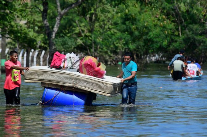 Dos hombres cargan una cama en barriles flotantes en una carretera inundada por la tormenta Eta el 8 de noviembre de 2020 en Rio Nance, Honduras.