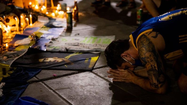 Un seguidor se arrodilla frente a una ofrenda mientras rinde homenaje a la exestrella del fútbol Diego Maradona.