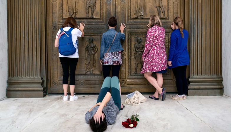 26 de septiembre – Mujeres conservadoras que apoyaron la nominación de Amy Coney Barrett a la Corte Suprema oran mientras tocan las puertas de la corte en Washington. Una mujer yace en el suelo cerca, de luto por la muerte de la jueza Ruth Bader Ginsburg. Erin Schaff / The New York Times / Redux