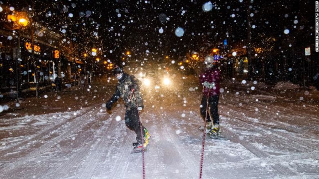 Snowboarders viajan detrás de una SUV mientras la nieve cae el 23 de diciembre de 2020 en Minneapolis, Minnesota.