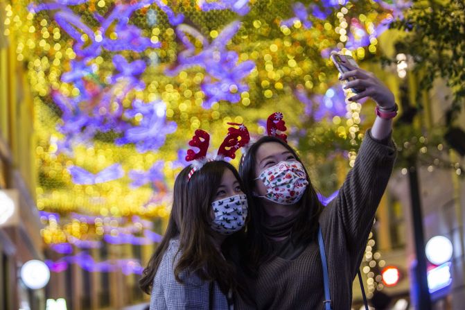 Dos mujeres que llevan mascarillas con motivos navideños se toman una foto cerca de una exposición navideña en un centro comercial del distrito de Wanchai, en Hong Kong, el 24 de diciembre de 2020.