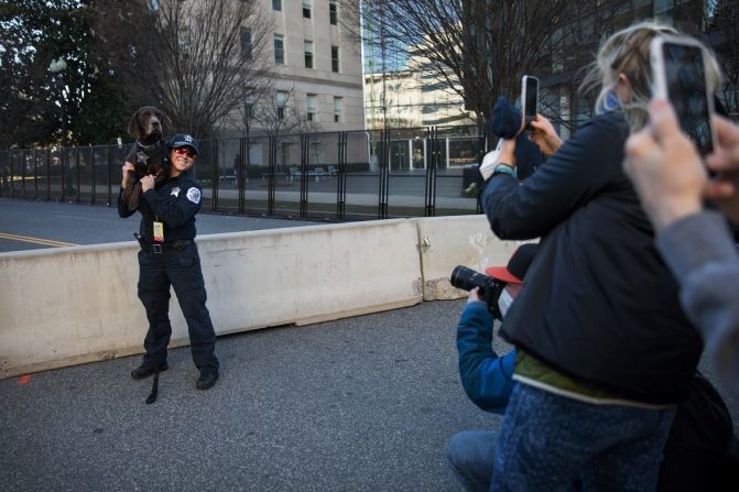 Personas toman fotos de un perro policía que posa con un agente afuera del Capitolio el martes 19 de enero.