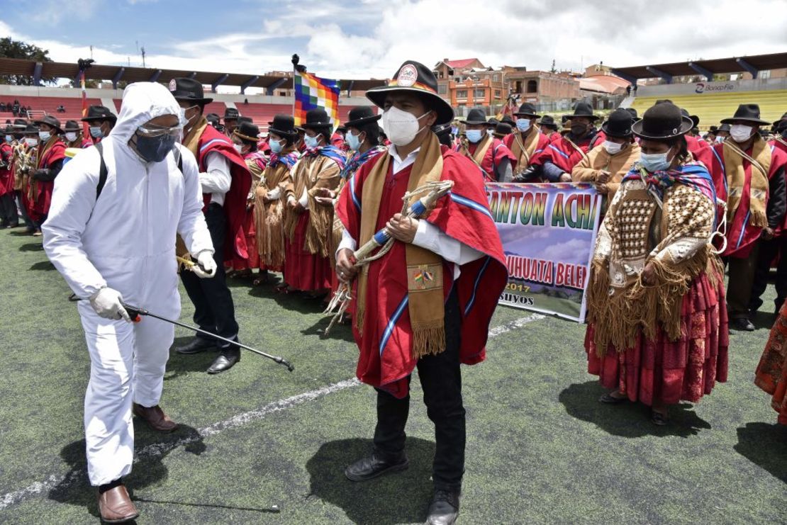 Un hombre con equipo de protección desinfecta a indígenas aymara que participan en la conmemoración del 195 aniversario de la creación de la provincia Omasuyos, sede de la organización campesina Ponchos Rojos, en Achacachi, Bolivia.