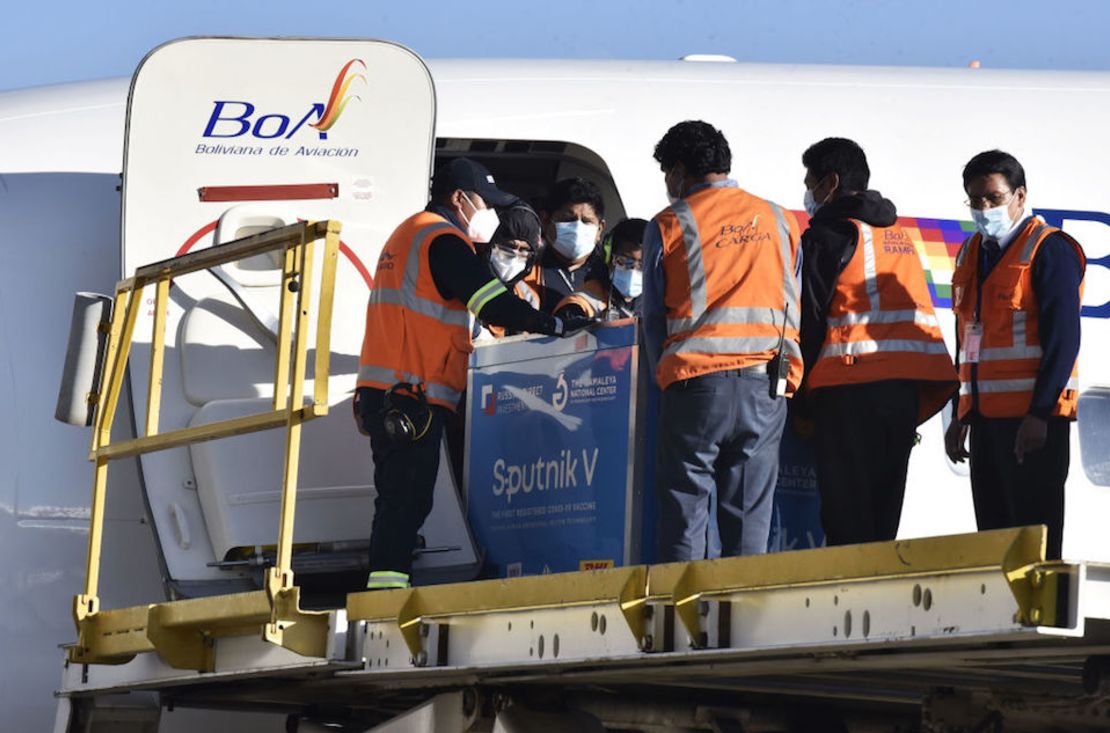 Trabajadores aeroportuarios manejan una caja con un lote de vacunas Sputnik V en el Aeropuerto Internacional El Alto en La Paz, Bolivia. (Photo by AIZAR RALDES / AFP)