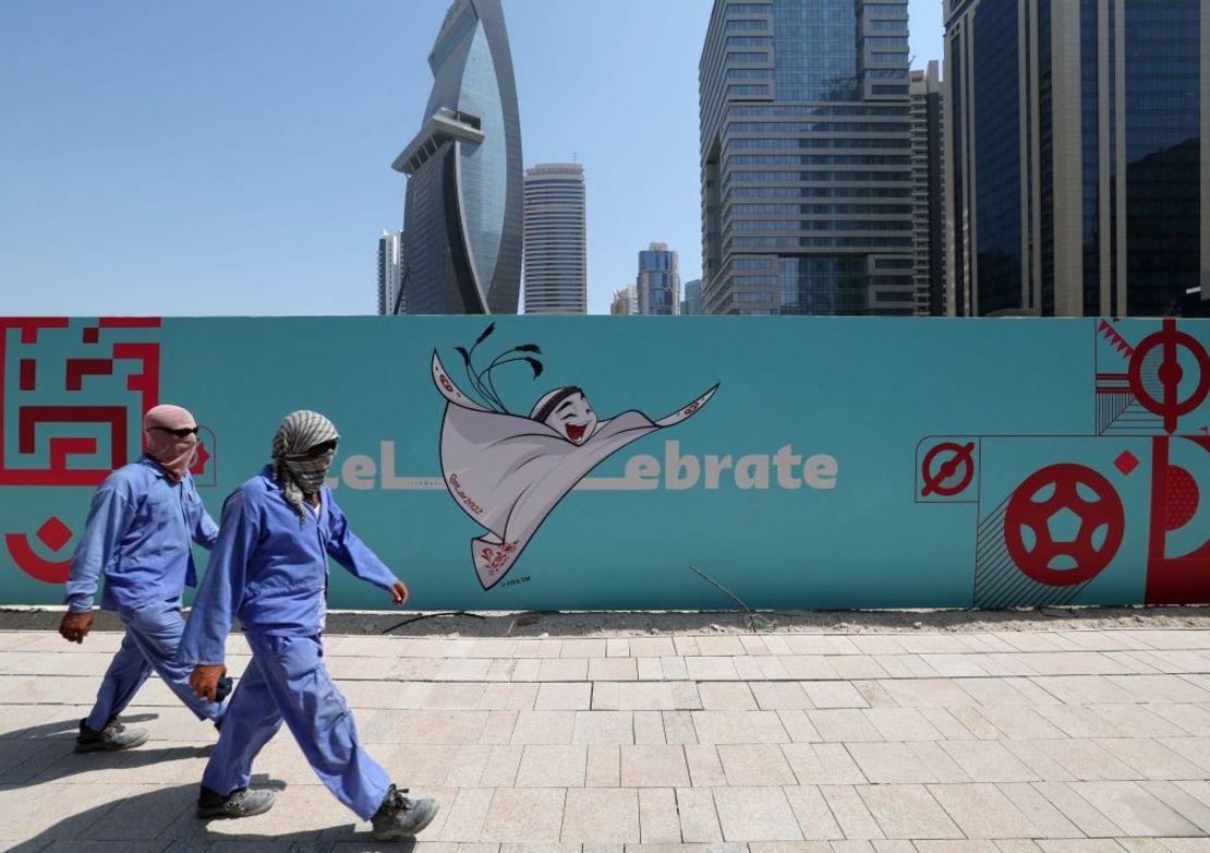 Trabajadores pasan frente a una valla publicitaria que muestra una ilustración de la mascota de la Copa Mundial de la FIFA Qatar 2022 "La'eeb" en la capital de Qatar, Doha, el 13 de octubre de 2022