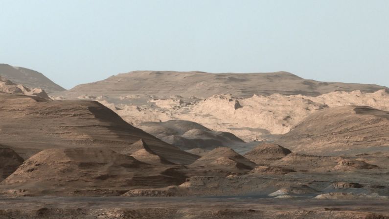 Esta imagen compuesta, cuyo horizonte son las regiones más altas del Monte Sharp, fue tomada en septiembre de 2015 por el rover Curiosity de la NASA. En primer plano hay una larga cresta repleta de hematita. Un poco más allá hay una llanura ondulada rica en minerales arcillosos. Y un poco más al fondo se encuentra una multitud de cerros redondeados, todos ricos en minerales de sulfato. La mineralogía cambiante en estas capas sugiere un entorno que se modificó en los inicios de Marte, aunque todas involucran exposición al agua hace miles de millones de años.
