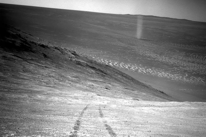 Desde su posición en lo alto de una cresta, el Opportunity grabó en 2016 esta imagen de un remolino de polvo en Marte recorriendo valle. La foto también capta las huellas del rover que conducen a la pendiente norte de Knudsen Ridge, que forma parte del borde sur del Valle de Marathon.