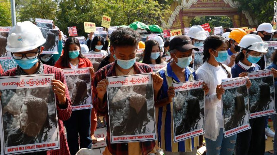 Estudiantes de la Universidad de Mandalay inclinan la cabeza mientras sostienen carteles con imágenes de Mya Thweh Thweh Khine el 14 de febrero de 2021.