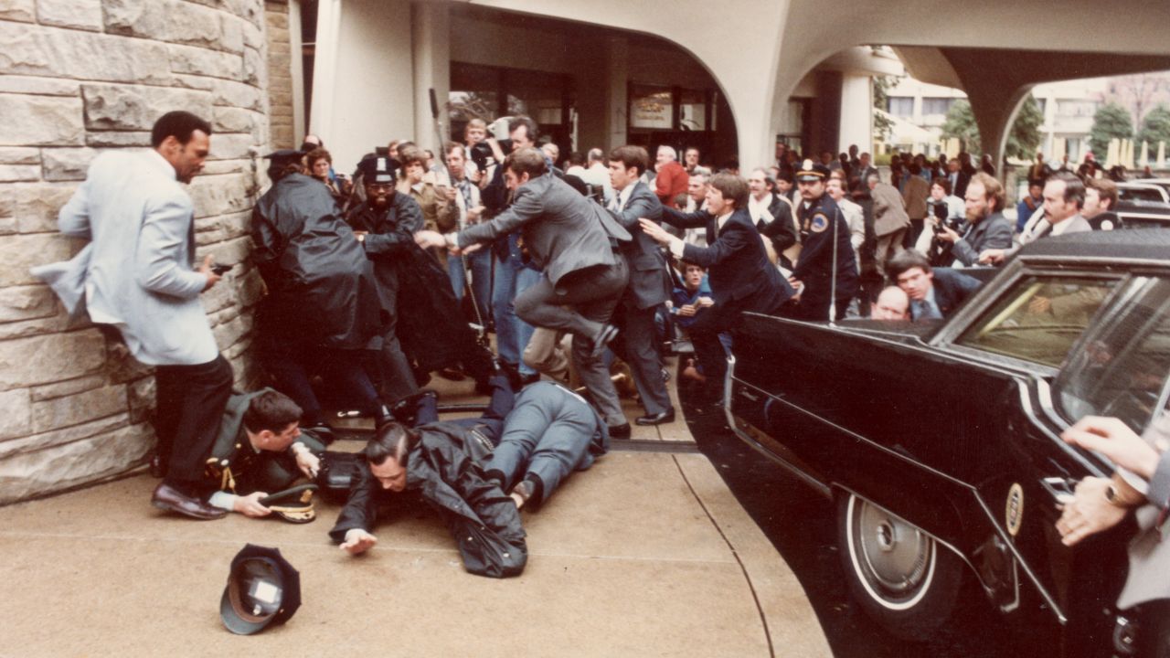 View of police officers and Secret Service agents as they dive to protect President Ronald Reagan amid a panicked crowd during an assassination attempt (by John Hinckley Jr) outside the Washington Hilton Hotel, Washington DC, March 30,1981.