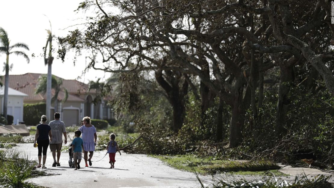 Una familia camina por una calle llena de ramas caídas en Marco Island, Florida.