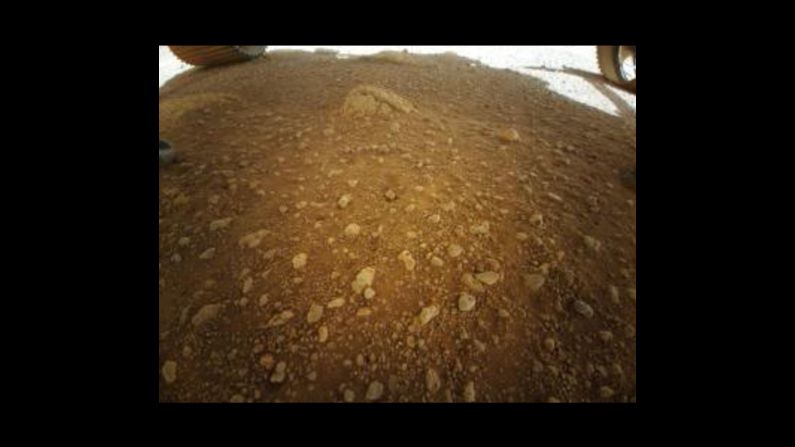 Esta es la primera imagen a color que tomó el helicóptero Ingenuity de Marte. A pesar de su baja resolución, se puede observar el suelo del cráter Jezero en Marte y una parte de dos ruedas del rover Perseverance. Se espera que Ingenuity logre fotos de mayor resolución durante sus vuelos de prueba.
