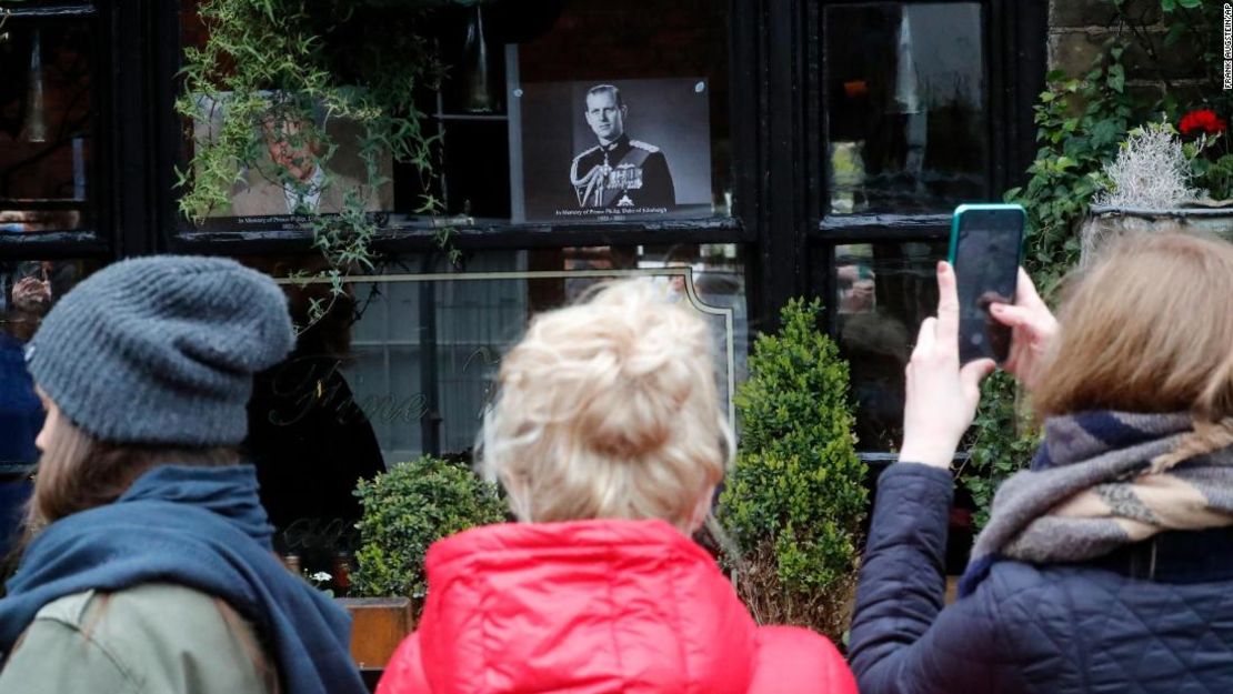 La gente toma fotos de un retrato del príncipe Felipe en la ventana de un pub cerca del Castillo de Windsor el sábado.