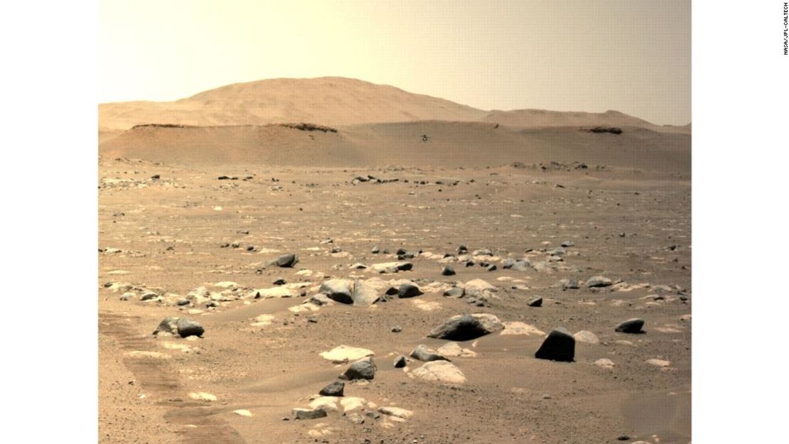 El rover Perseverance usó una de sus cámaras para capturar Ingenuity durante su tercer vuelo el domingo. Se puede ver cerca del centro de la imagen, volando sobre las rocas del aeródromo.